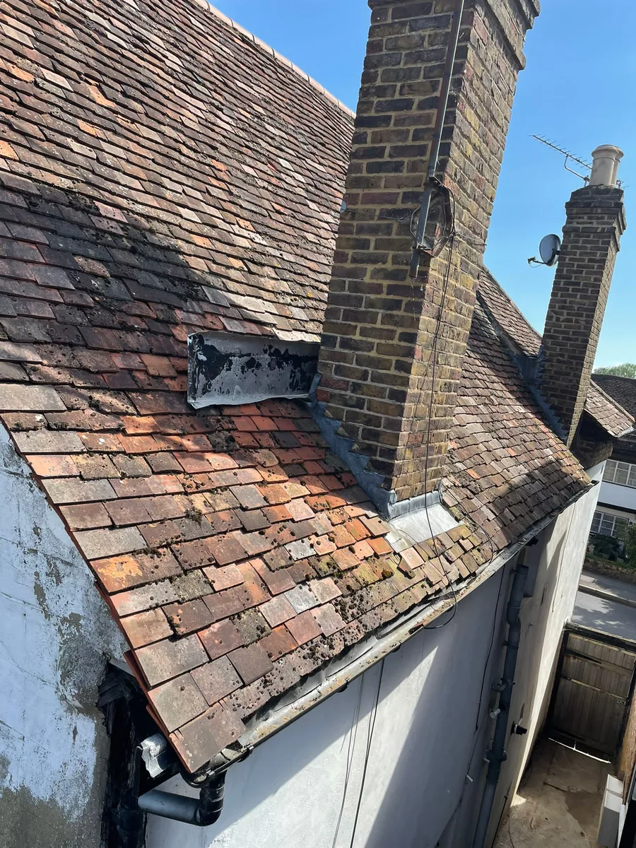 Deteriorated plain clay tile roof with failed flashing around chimney — before remedial work